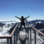 A woman stands on a viewing platform in Vysok&eacute; Tatry, Slovakia, surrounded by clouds and mountains, embracing freedom.