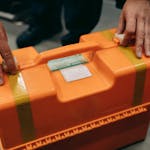 Close-up of hands holding an orange emergency medical kit indoors.